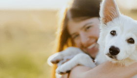 A woman lovingly hugs her white dog in a sunlit field, highlighting the bond between pets and their people.
