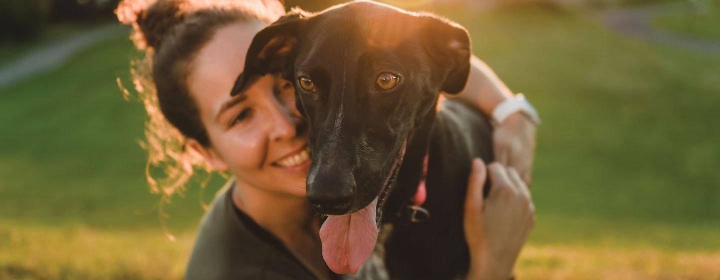 Smiling woman hugging her happy black dog at sunset, symbolizing the personal impact of pet cancer and the importance of community fundraising to Stop Cancer Furever.